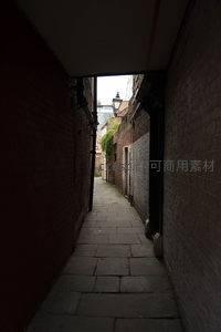 幽深窄巷光影对比强烈，砖墙夹道通向亮处街灯与建筑，神秘静谧