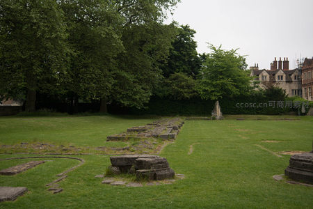 绿茵草坪上的古老石基遗址，背景掩映于浓密树丛与宅邸