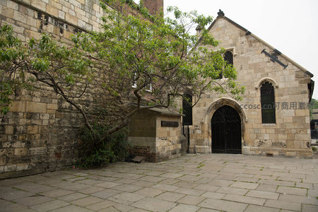石砌教堂侧院，古树斜倚墙垣，黑铁门与彩窗映衬厚重历史