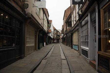 约克古城窄巷清晨静谧街景，石板路两旁老店招牌林立
