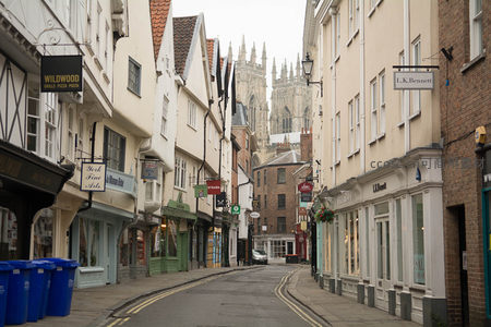 约克石板街远眺大教堂，两旁商铺林立蓝桶点缀，晨光微照古街静谧