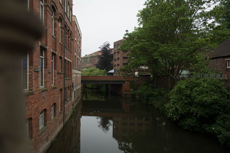 红砖建筑沿河而立，小桥横跨静谧水道，绿树倒影如画