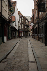 狭窄鹅卵石巷道曲折延伸，两侧老屋悬挂复古招牌，雨后微湿显古意