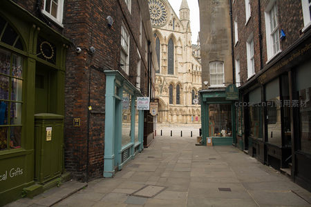 约克大教堂尖塔与玫瑰窗映衬下，古巷尽头商铺林立，绿窗蓝门错落有致