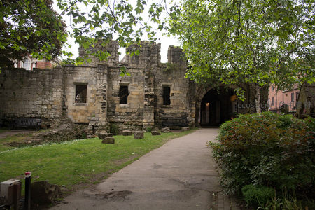 古老石墙遗迹掩映在绿树丛中，青草小径通向拱门入口