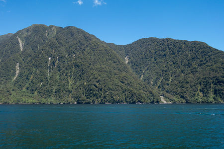 碧蓝湖面映衬苍翠山峦，陡峭森林覆盖崖壁，晴空万里无云