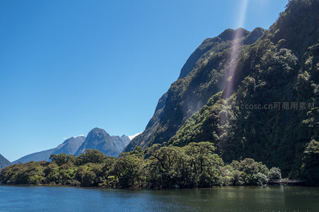 阳光穿透林间洒落湖面，远山雪峰与近处绿崖相映成趣