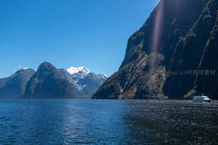 雪山远眺峡湾碧水，游船穿行光影洒落崖壁