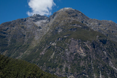 雄伟山峰顶覆薄雪，岩层褶皱与林带分明展现地质力量