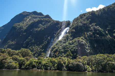 峡湾高崖瀑布飞泻而下，阳光穿透水雾形成光柱奇观