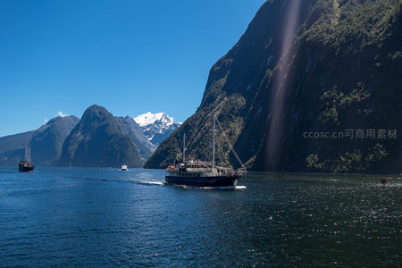 峡湾巨壁下帆船巡游，阳光穿透云隙洒向碧波