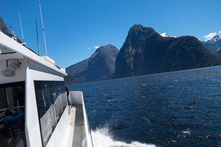 游船航行于峡湾之间，游客倚栏远眺巍峨峰峦与碧海晴空