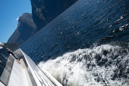 游艇疾驰于峡湾碧波之上，激起雪白浪花与陡峭岩壁相映成趣