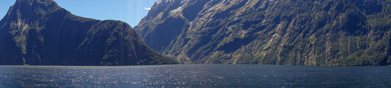 米尔福德峡湾全景：巍峨群峰环抱幽深水域，绿植覆崖倒影如画