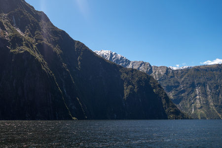 雪顶群峰与墨绿峡湾交响：远山积雪未融，近岸植被葱郁，光影交错