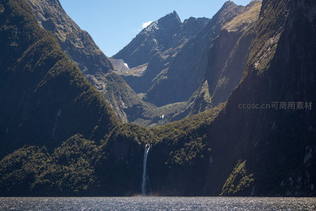 米尔福德峡湾日光穿透峰谷，瀑布飞流直下汇入幽蓝海湾