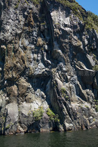 深色花岗岩崖壁矗立于碧水之畔，展现大自然雕琢的磅礴力量