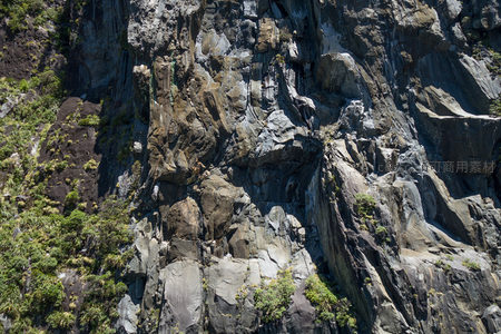 陡峭岩壁纹理细节航拍，青苔点缀灰褐层理岩石