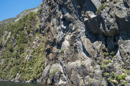 峡湾边巨型岩壁全景，绿植覆盖斜坡与裸露岩面形成壮丽对比