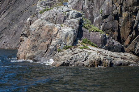 海岸岩礁边缘浪花拍打，岩面斑驳处可见小型太阳能板装置