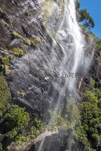 垂直悬崖间激流飞泻，水珠在光线下晶莹闪烁，岩层纹理清晰，植被顽强附生其上