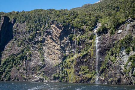 峡湾巨崖上多级瀑布垂挂，绿植覆被与深色岩层形成强烈对比