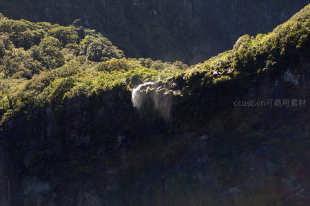 阳光穿透云雾洒落悬崖瀑布，绿植覆盖岩壁生机盎然
