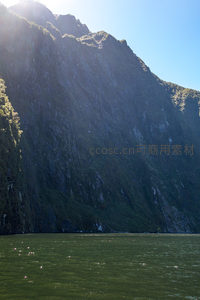 晨光穿透云隙照亮峡湾岩壁，水面浮光跃金，生机盎然