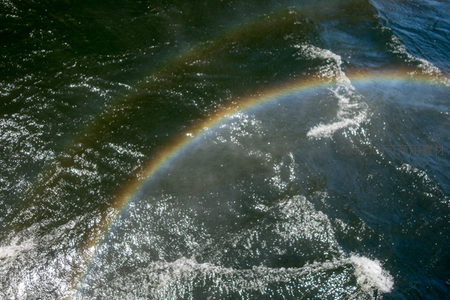 水面波光中浮现完整弧形彩虹，阳光洒落粼粼水纹，构成诗意自然画卷。
