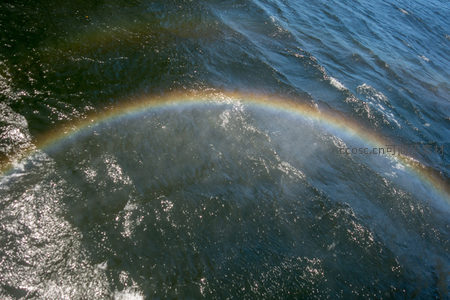 海面浪涌间悬浮半圆彩虹，阳光穿透水雾形成七彩光带，宁静而神秘。