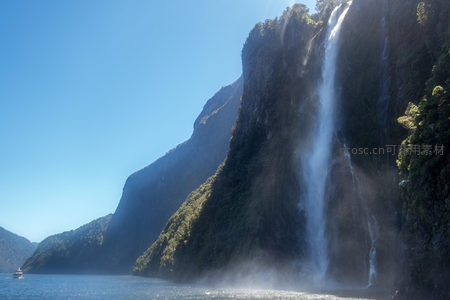 米尔福德峡湾瀑布倾泻入海，陡峭岩壁覆满绿植，蓝天映衬壮丽景观