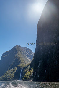 逆光拍摄峡湾瀑布群，阳光穿透云隙洒向碧水深渊