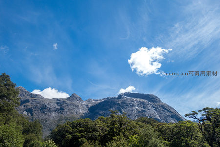 巍峨雪山耸立蓝天之下，云絮轻绕峰顶，林海苍翠铺展山脚