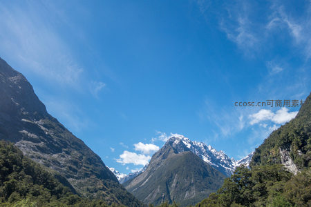 V型山谷环抱雪峰，蓝天白云映衬苍翠林带，壮丽全景尽收眼底