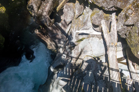 峡谷顶视视角：激流奔涌于巨岩裂隙，枯木投影如几何图案