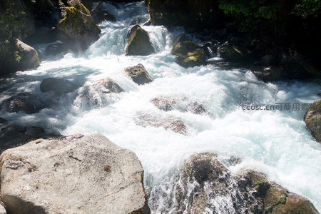 阳光下的山溪奔涌穿石，浪花翻腾气势磅礴