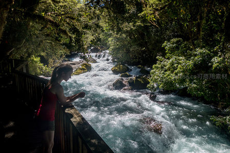 女子凭栏静观湍流，林间栈道与奔涌溪水构成人与自然和谐对话画面
