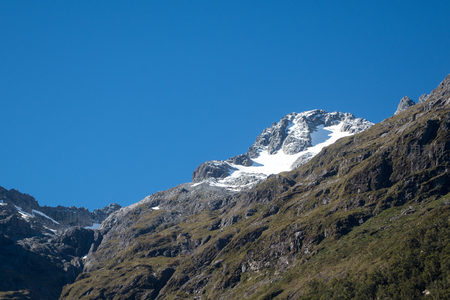 雪顶山峦傲立晴空，草甸斜坡延伸至岩壁，明暗交界处生机盎然
