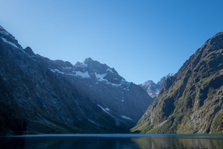 碧蓝湖面倒映巍峨雪峰，峡谷两侧绿植覆盖，晴空万里无云