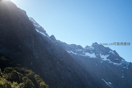逆光下的雪岭峻峰，阳光勾勒岩层棱角，林线以下绿意盎然
