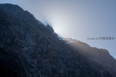 暮色中云隙透光洒落山峦，雪线隐现，岩壁阴影深邃苍茫