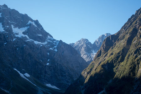 晨光映照雪线以下岩壁与林带的高山峡谷景致