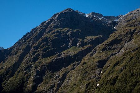晴空下苍翠山峦层叠，岩隙间残雪斑驳点缀