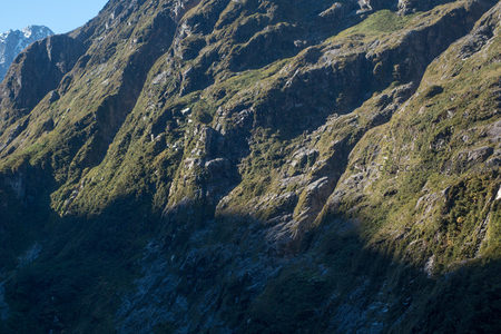 阳光斜照下的陡峭山崖，青苔与岩层交织成自然纹理画卷