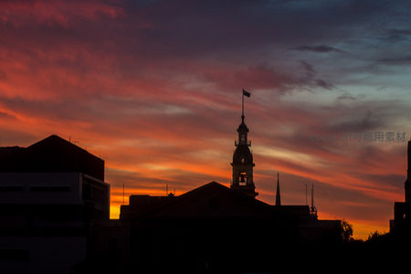 钟楼剪影立于绚烂晚霞中，国旗迎风飘扬