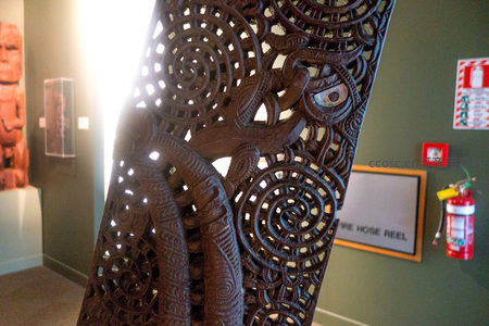 毛利木雕屏风特写：螺旋纹（Koru）与神话生物交织，嵌贝母点缀，光影流动