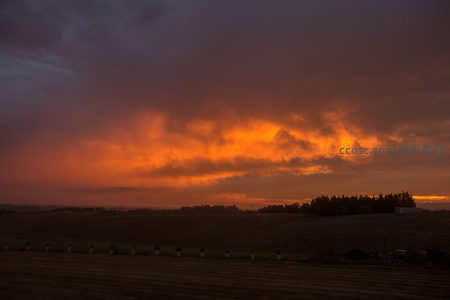 田野上空燃烧的晚霞云层，橙红烈焰映照收割后的麦田轮廓