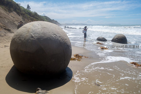 游客在摩拉基巨石滩与巨型球形岩石合影，海浪涌向岸边