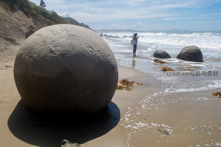 低角度拍摄摩拉基巨石近景，纹理清晰，游人涉水观石