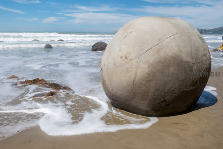 多颗摩拉基巨石散落海岸，潮汐退去留下湿润沙地与海藻痕迹
